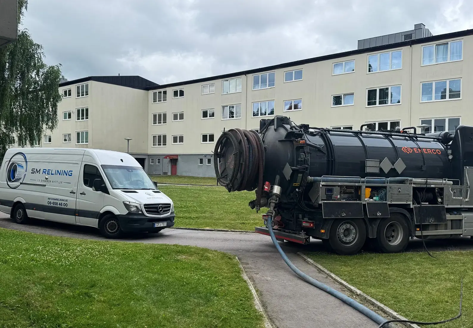 En SM Relining-skåpbil och en sugbil parkerade utanför ett flerfamiljshus.